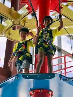 Two children in matching neon shirts stand in a colorful amusement ride, holding onto poles and smiling.