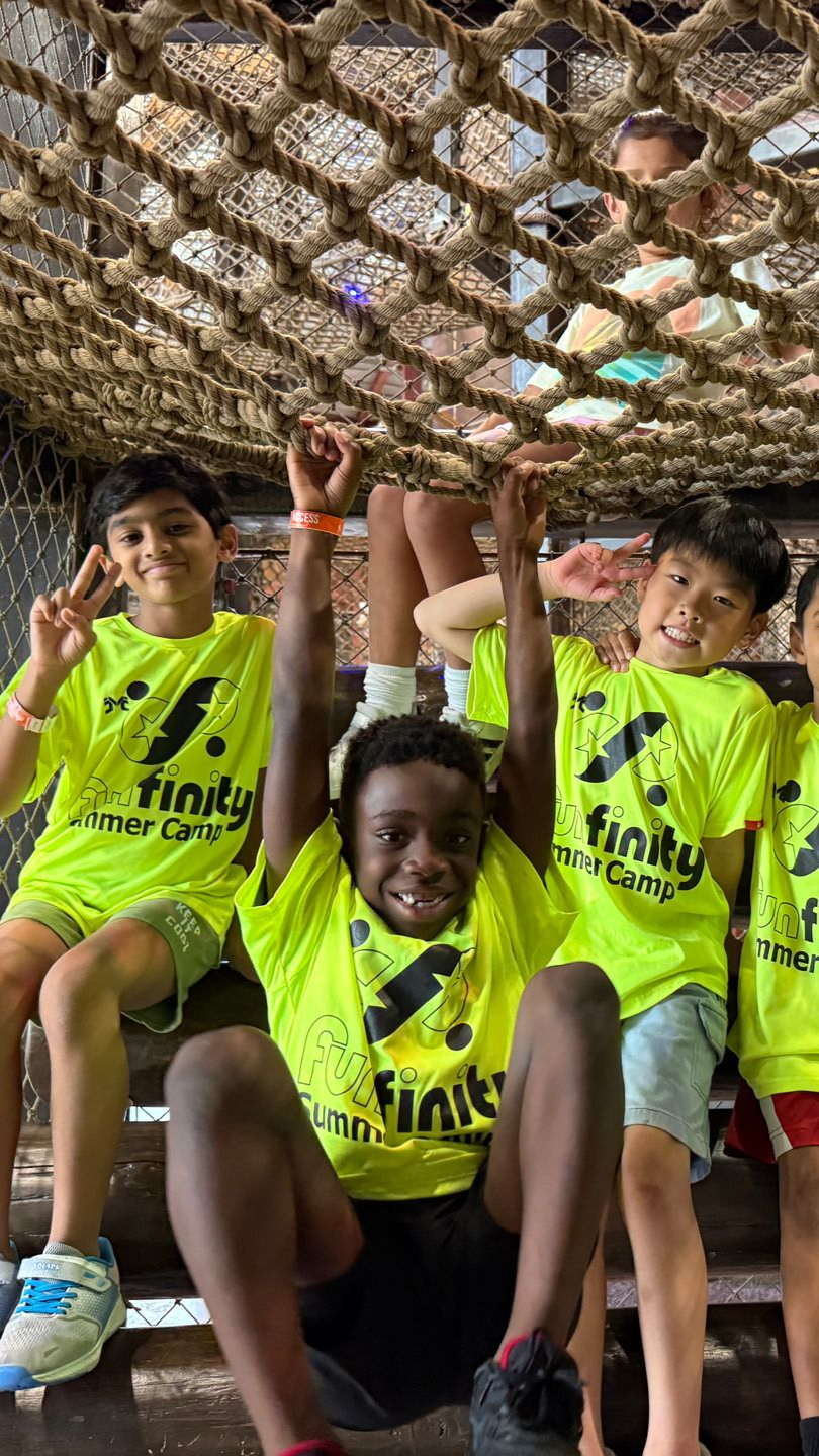 Youth soccer players in neon jerseys posing under a net canopy, smiling and making peace signs