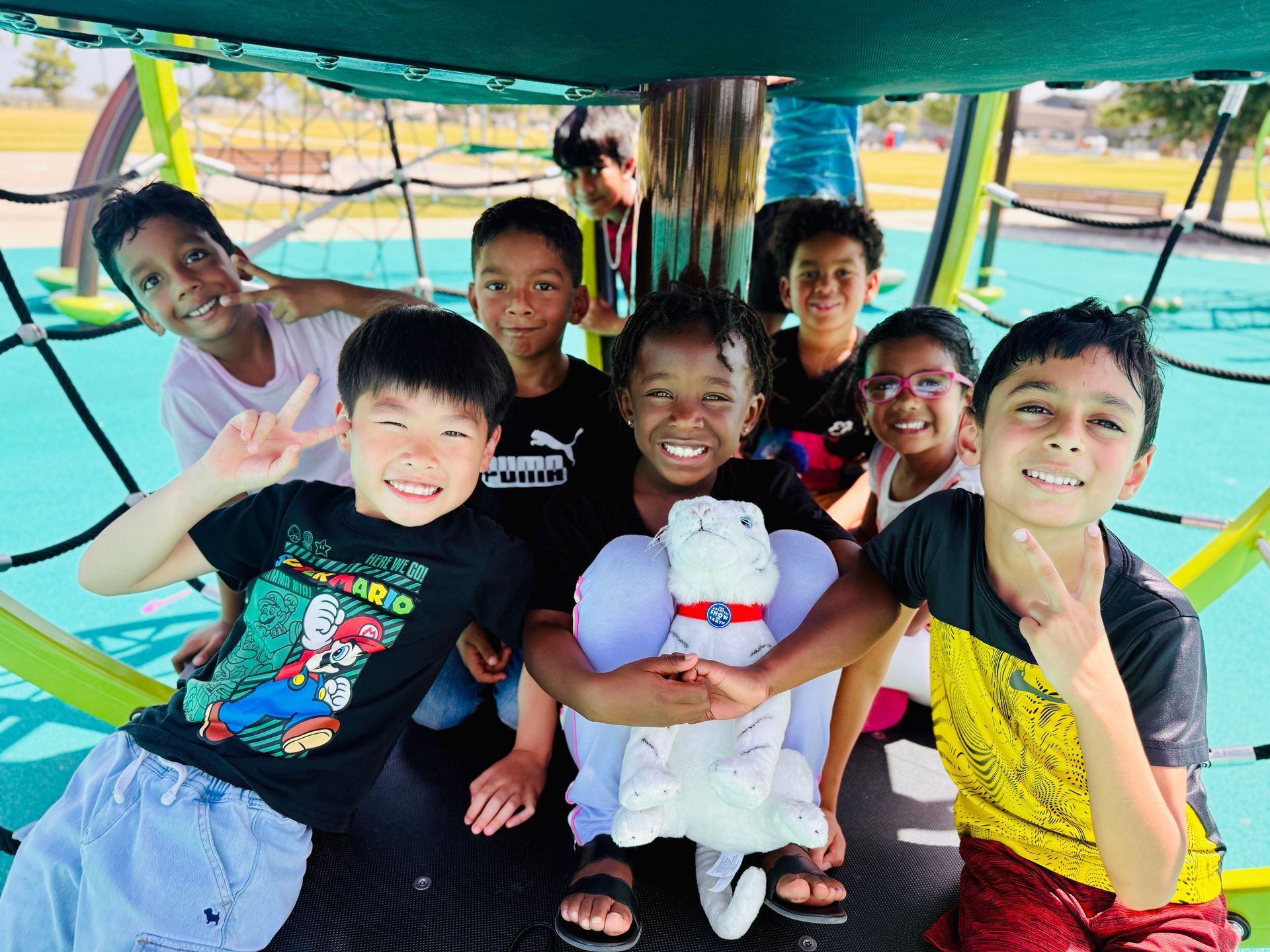 Children smiling and posing on a colorful amusement ride, one holding a stuffed animal