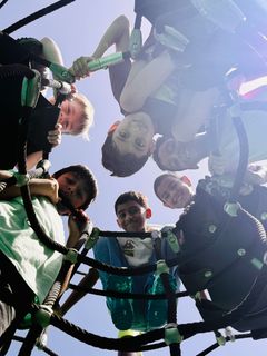 Group of people leaning over a circular net, looking down with bright sky above.