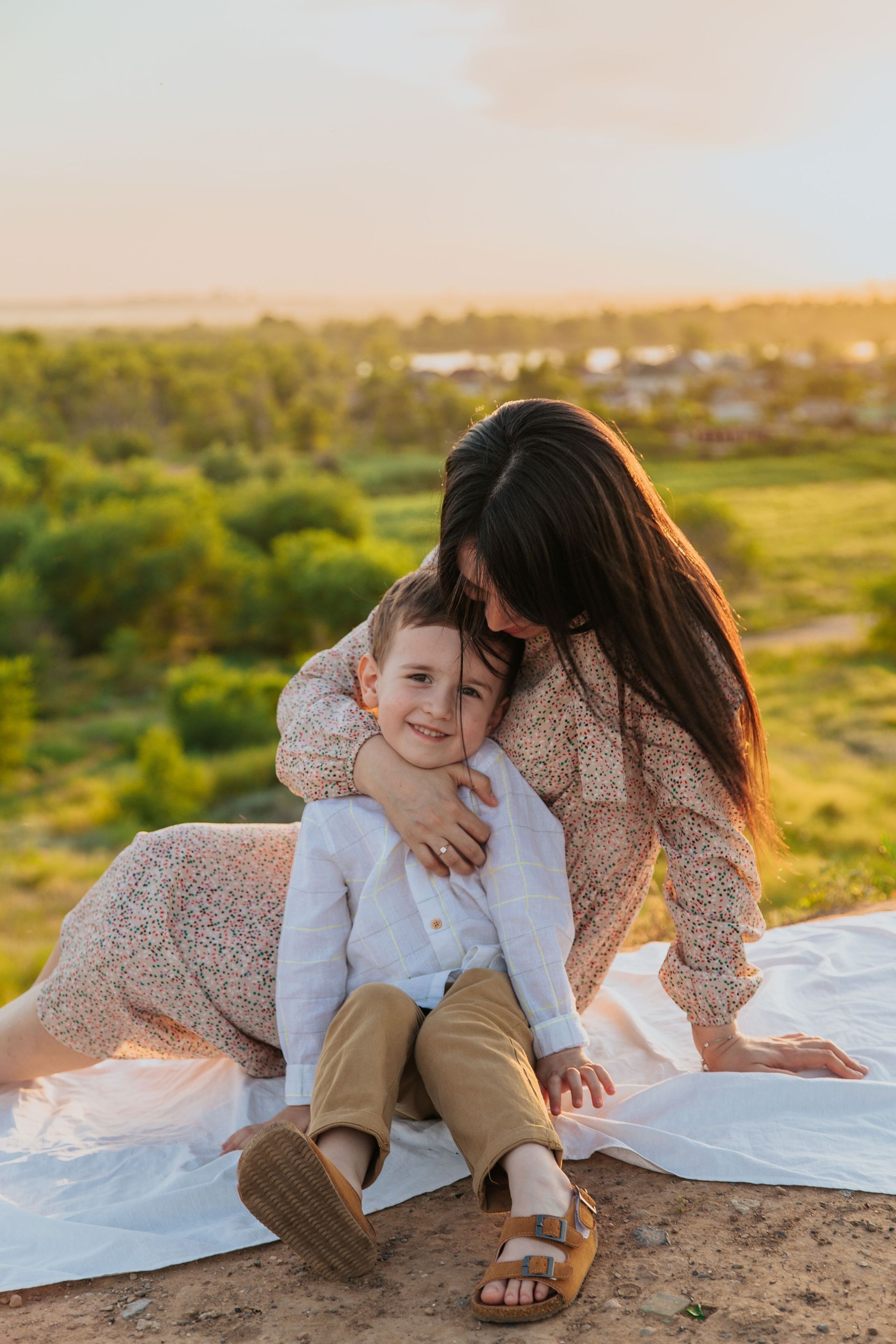Parent hugging child on a blanket at sunset in a grassy field
