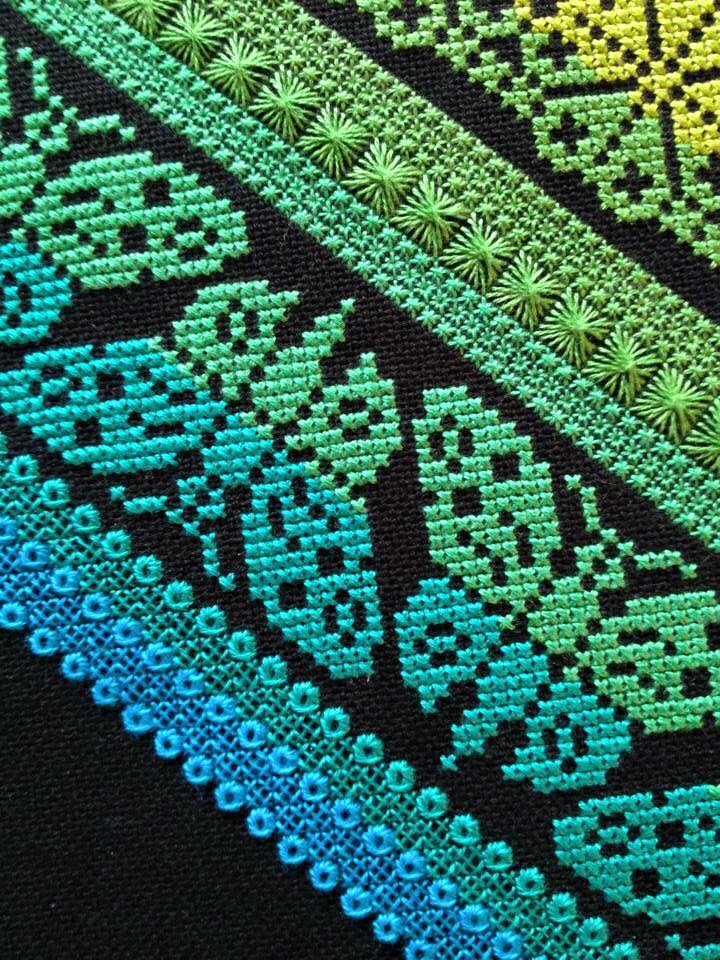 Intricate embroidery in an ombré of blue to green, featuring butterfly motifs and geometric borders on black fabric.