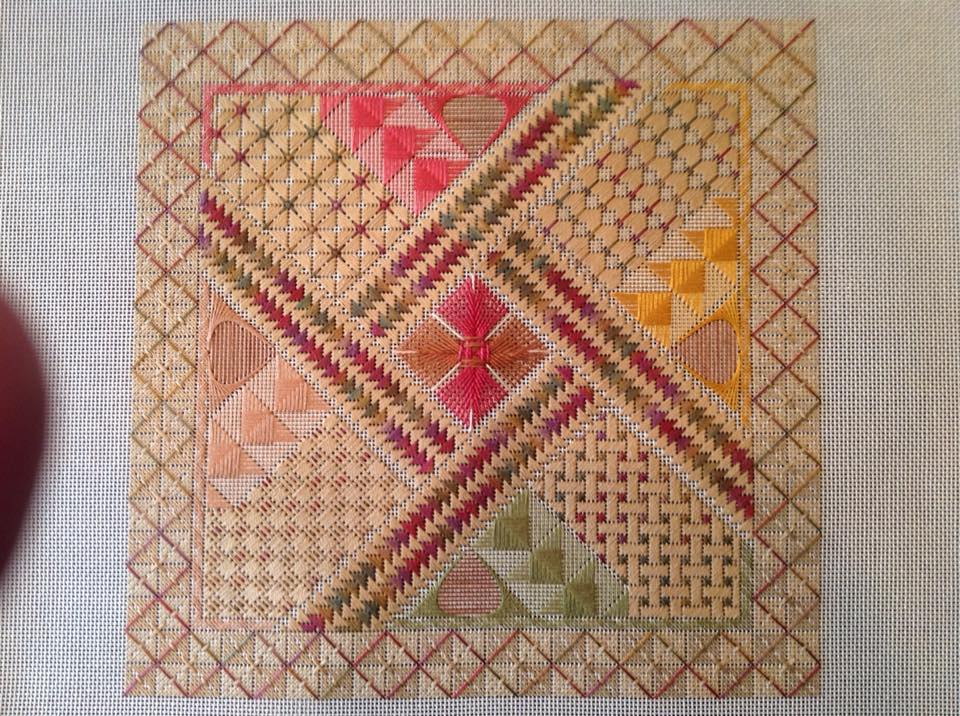 A square needlepoint piece with geometric patterns, diagonal braided lines, and a center star in red, gold, and green.