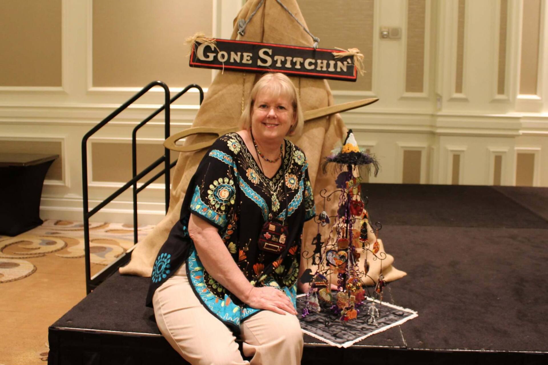 A woman sits on a stage next to a burlap-covered display topped with a 