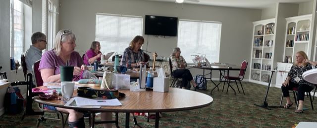 A group of people sit around round tables in a community room for a meeting or workshop.