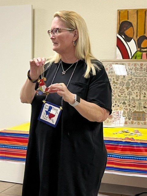 A person in a black shirt holds a small Texas-themed ornament while standing in front of a colorful, patterned tablecloth.