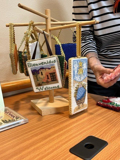 Handcrafted ornaments hang on a wooden display stand, including one featuring a Southwestern-style building.