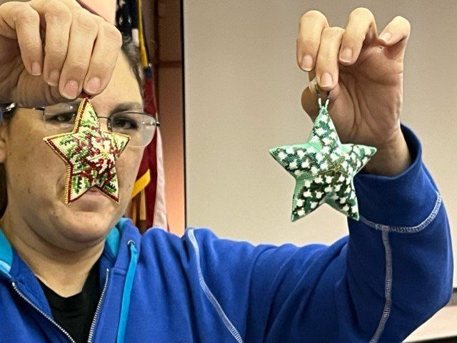 A person in a blue hoodie holds up two fabric star-shaped Christmas ornaments in front of their face.
