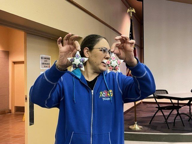 A person in a blue hoodie holds up two star-shaped decorations, one in each hand, in an indoor room.