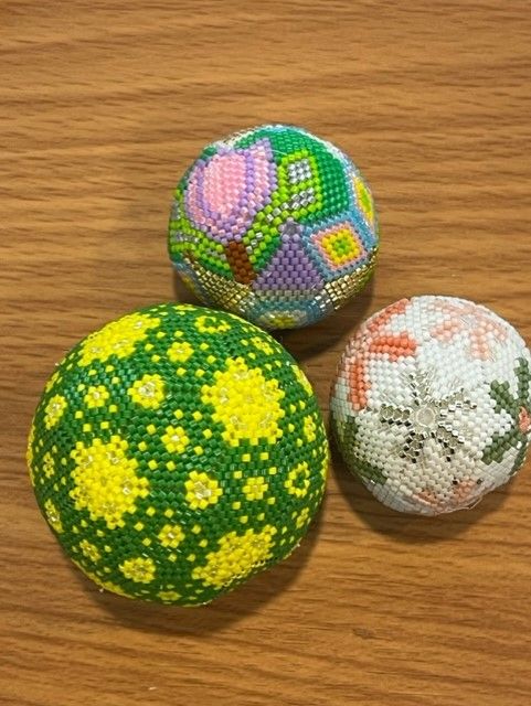 Three round, handmade beaded ornaments with geometric, floral, and snowflake patterns on a wood-grain surface.