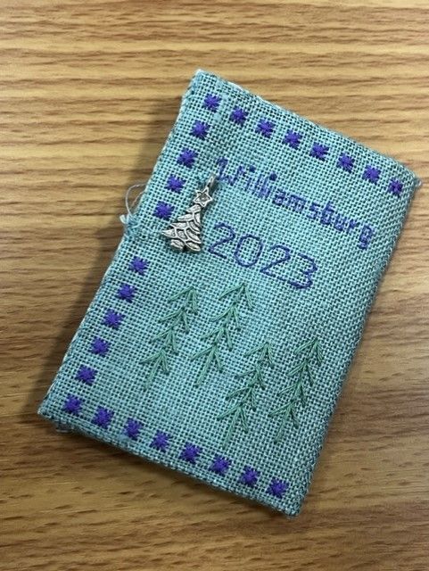 A small, light green fabric ornament embroidered with 
