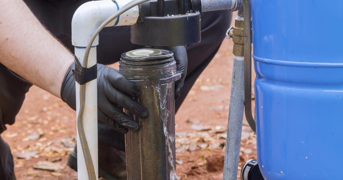 A man wearing black gloves is working on a water pump.