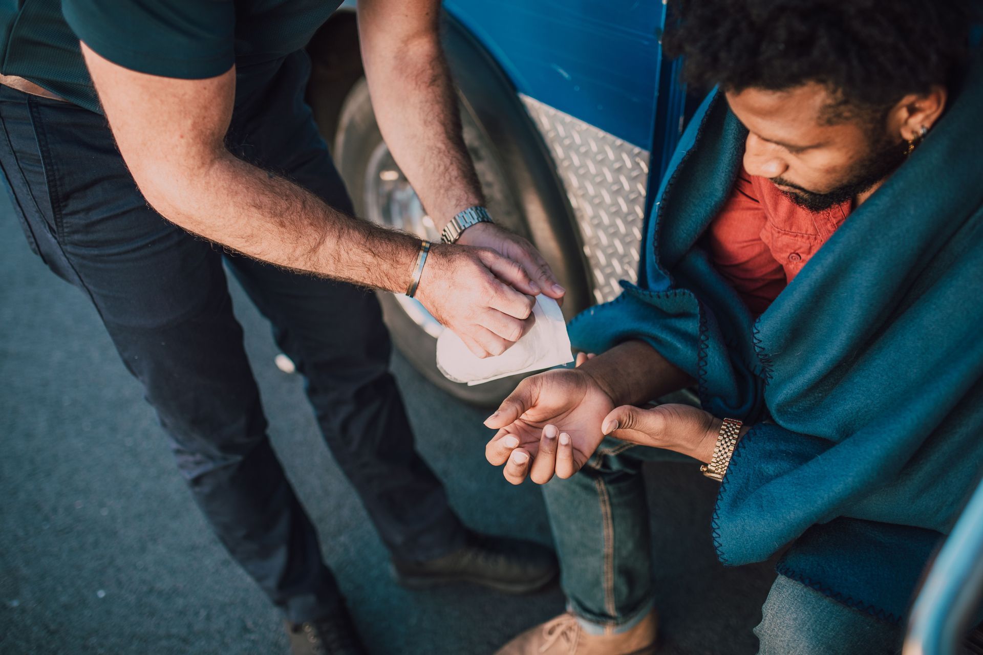 Two people wrapping a blue blanket around a seated person’s hands
