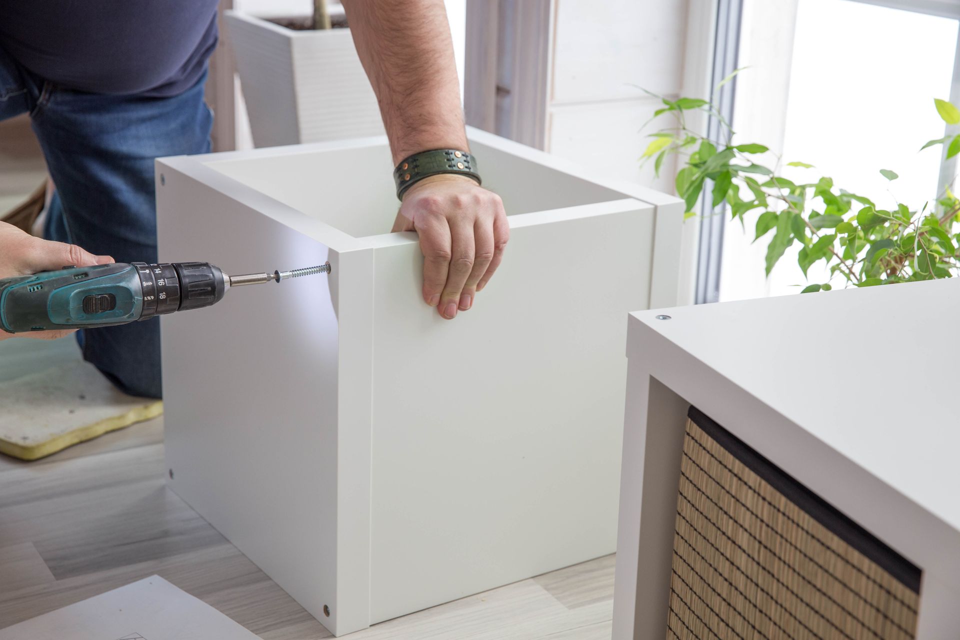 A man is using a drill to assemble a white box.