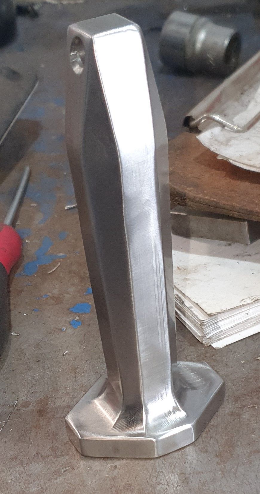A metal object is sitting on a table next to a screwdriver.