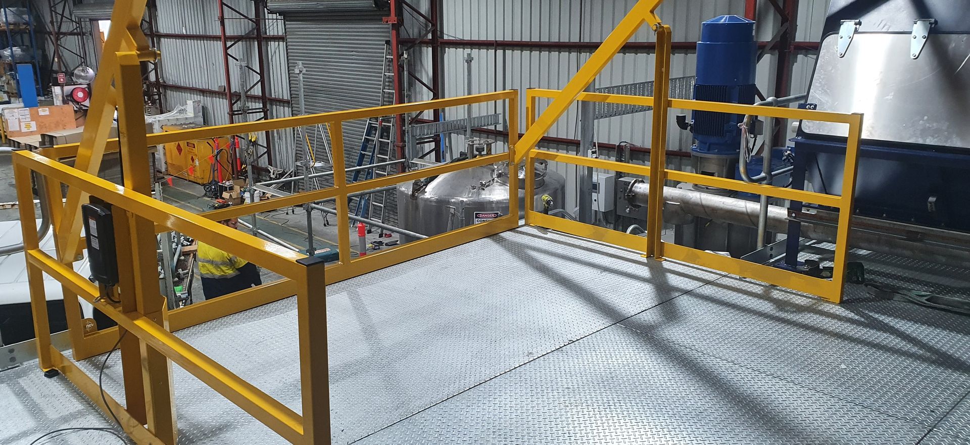 A yellow fence is surrounding a metal platform in a factory.