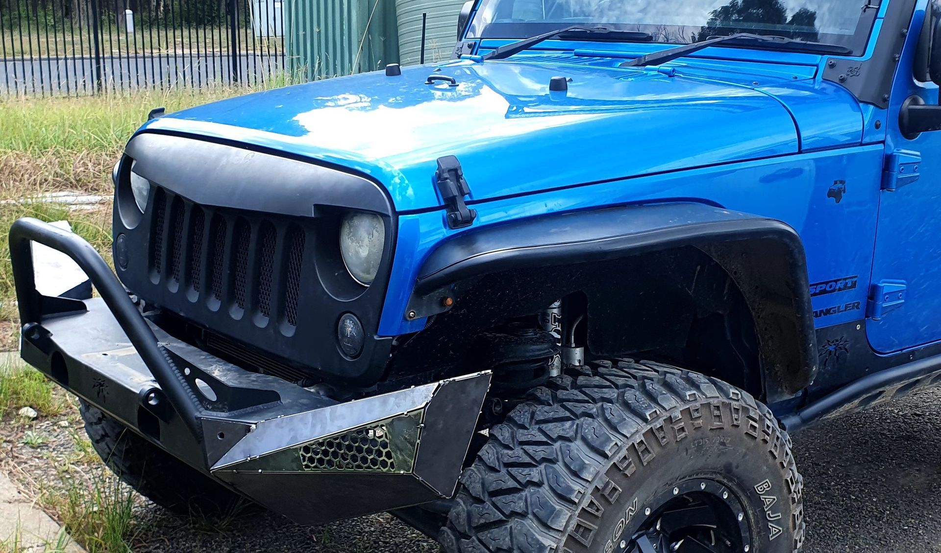 A blue jeep with a black bumper is parked on the side of the road.
