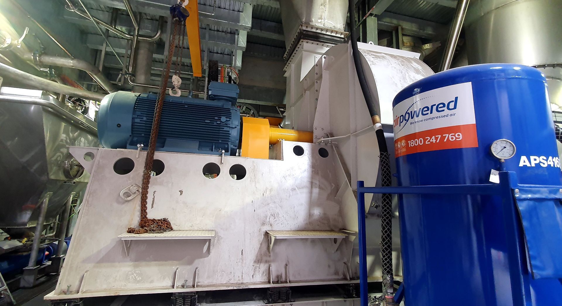 A large machine is being lifted by a crane in a factory.