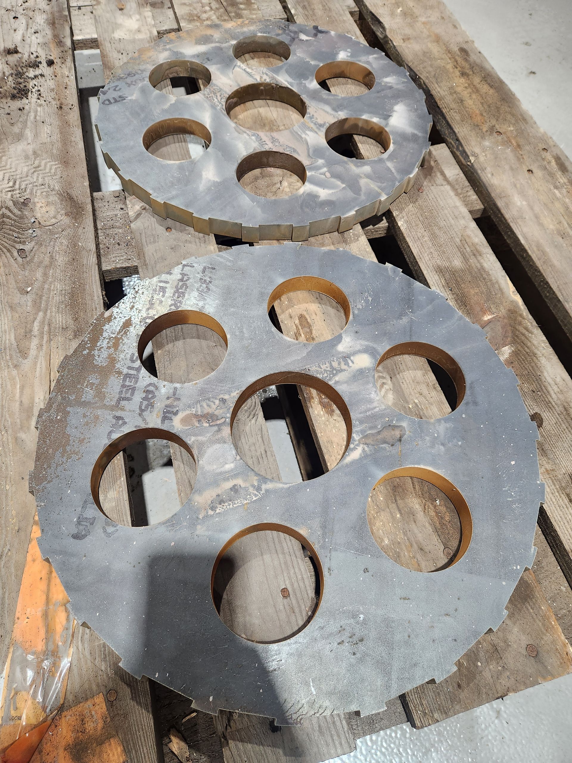 Two pieces of metal with holes in them are sitting on a wooden pallet.