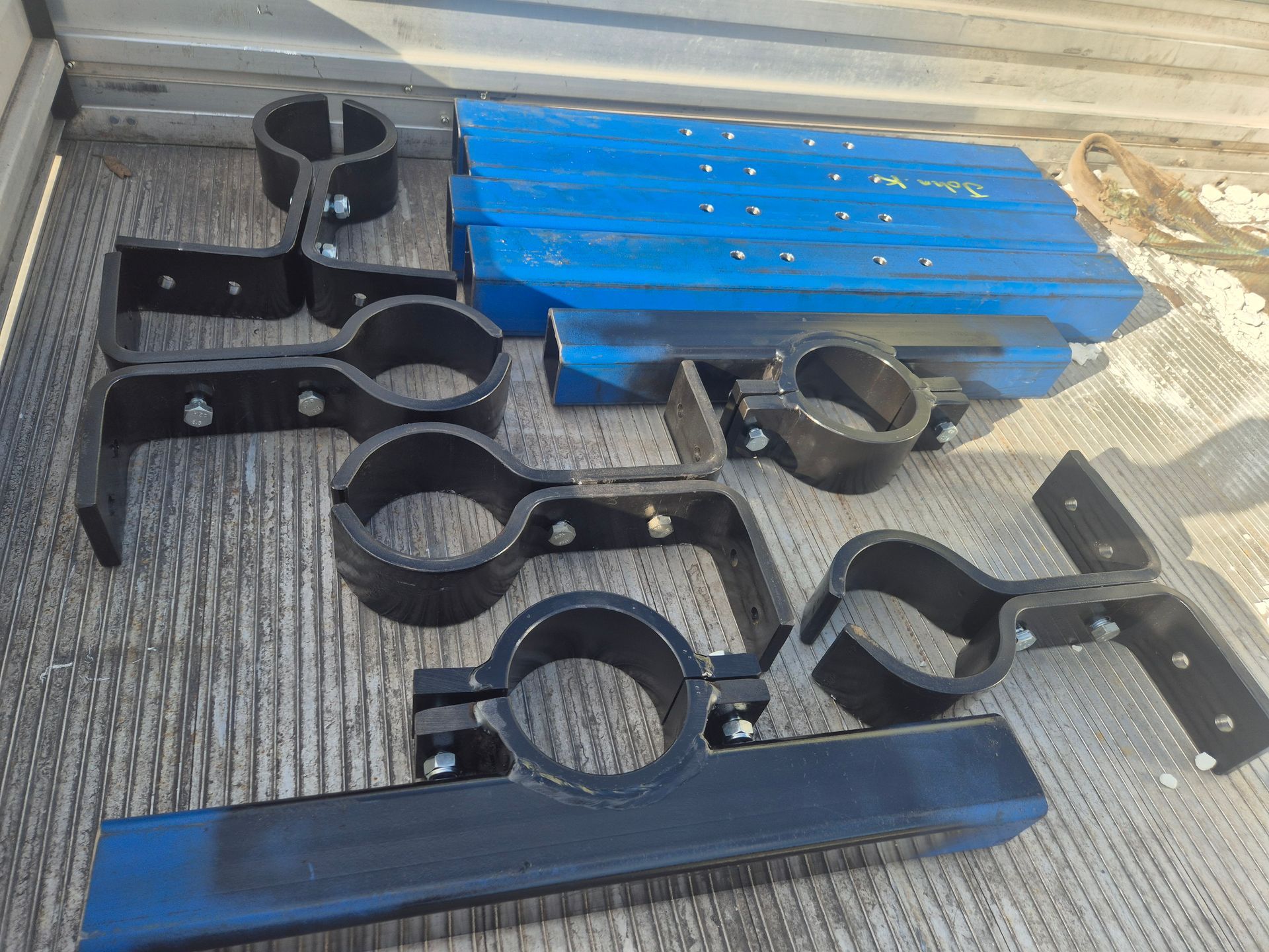 A bunch of metal pipe clamps are sitting on the ground next to a blue pallet.