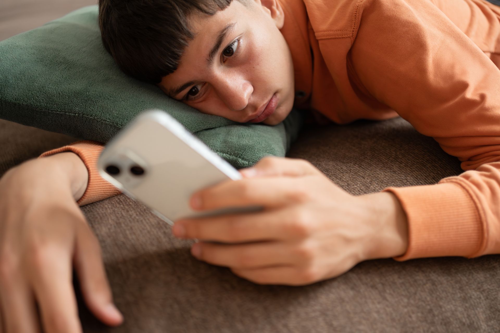 Person lying on a couch, looking at a white smartphone with a green pillow under their head.