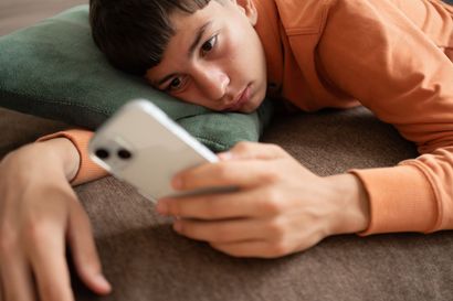 Person lying on a couch, holding a white smartphone and looking at the screen.