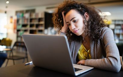 Person leaning over a laptop in a café, focused on the screen.