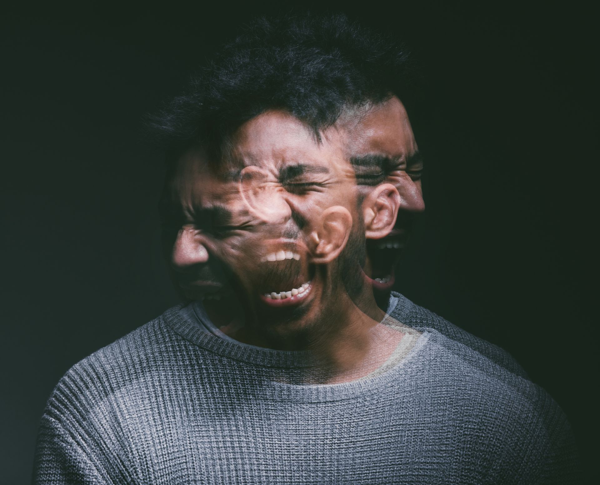 Blurred double exposure of a man in a gray sweater grimacing against a dark background