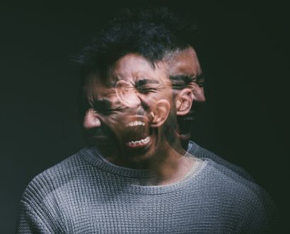 Blurred double-exposure portrait of a person grimacing against a dark background