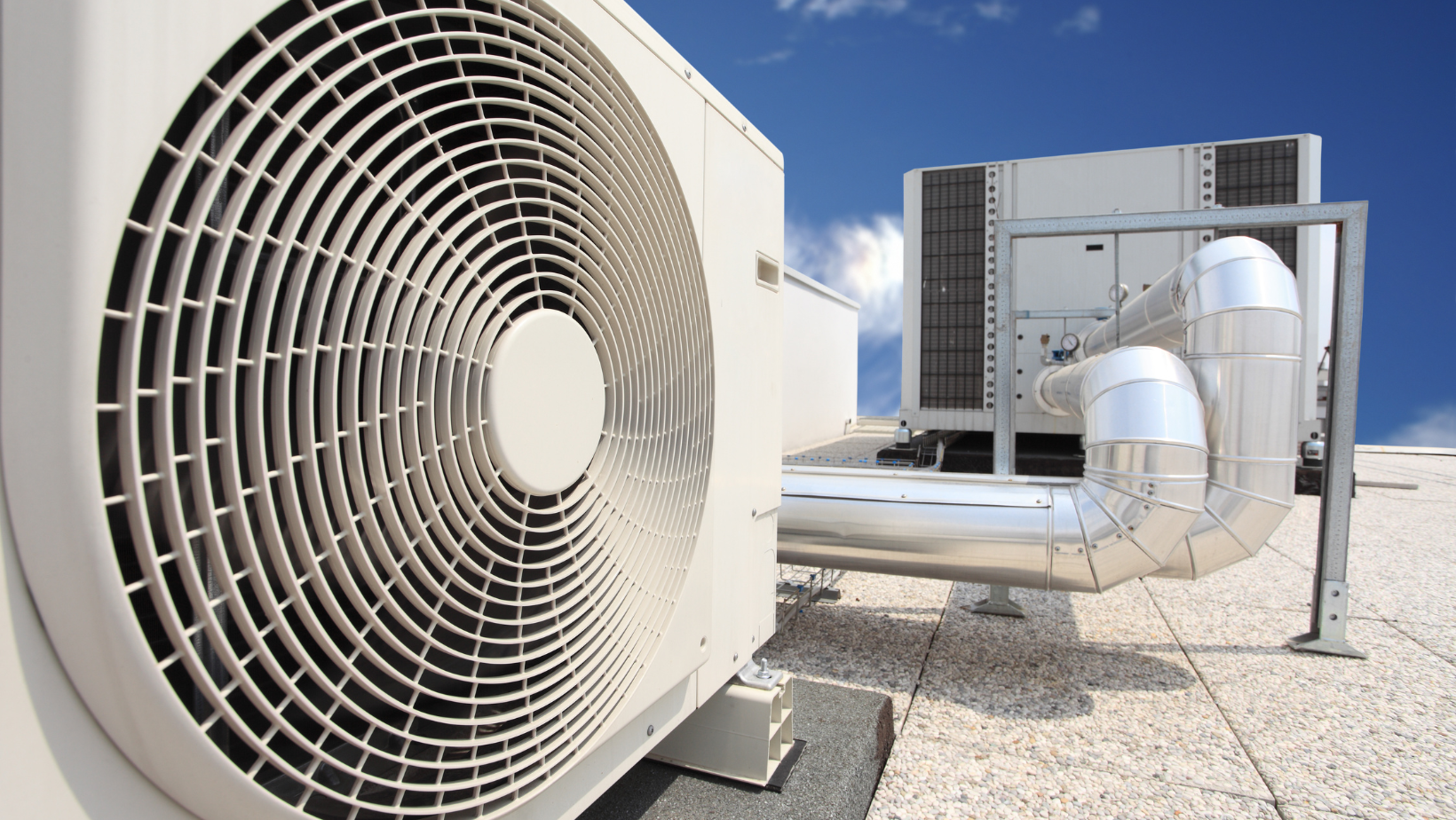 Rooftop HVAC condenser units with large circular fan and metal ducting under a clear sky