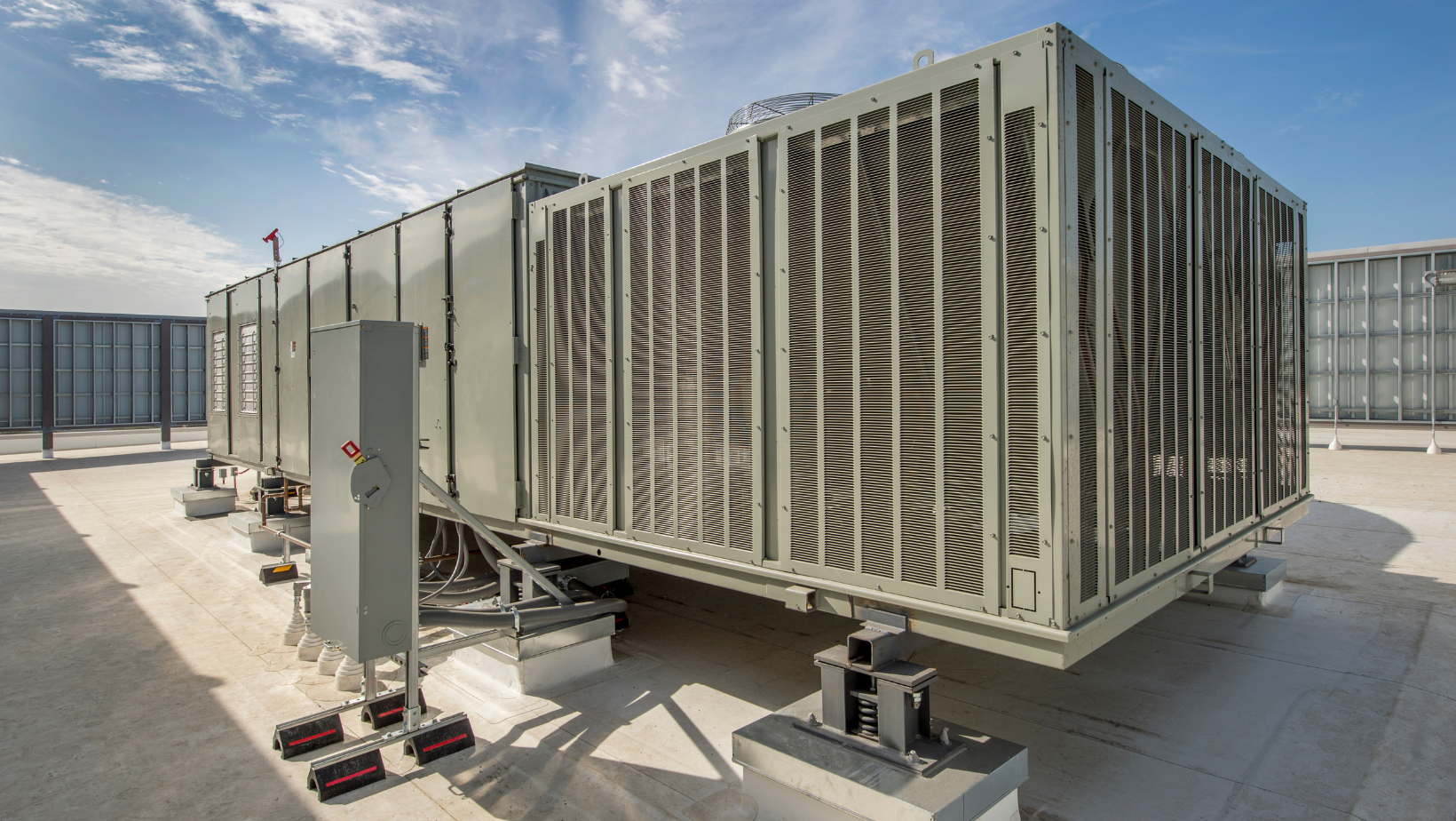 Row of large rooftop HVAC units with louvered metal panels on a flat industrial roof