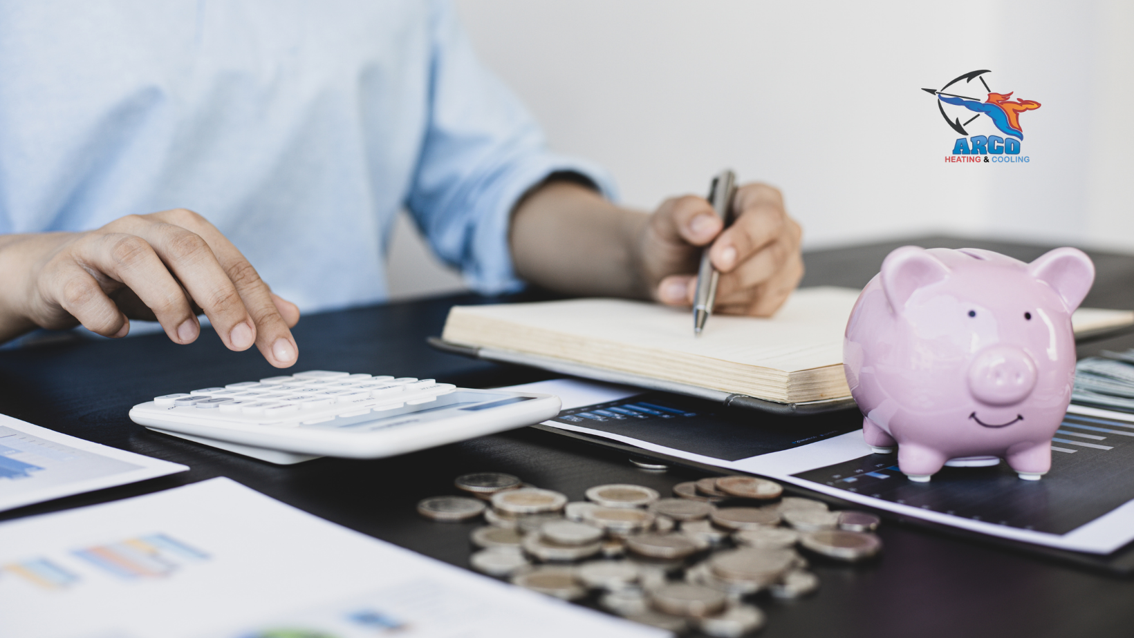 Person calculating finances with calculator, notebook, coins, and piggy bank on a desk.