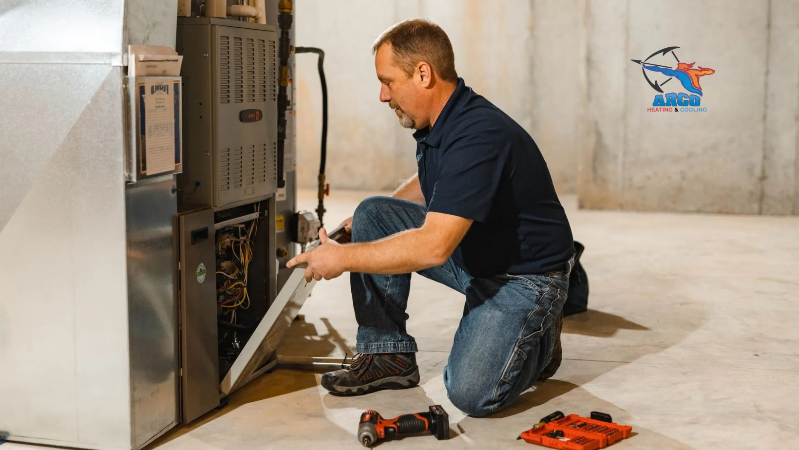 Technician repairs furnace in basement, examining wires with open panel. Red tools on floor.
