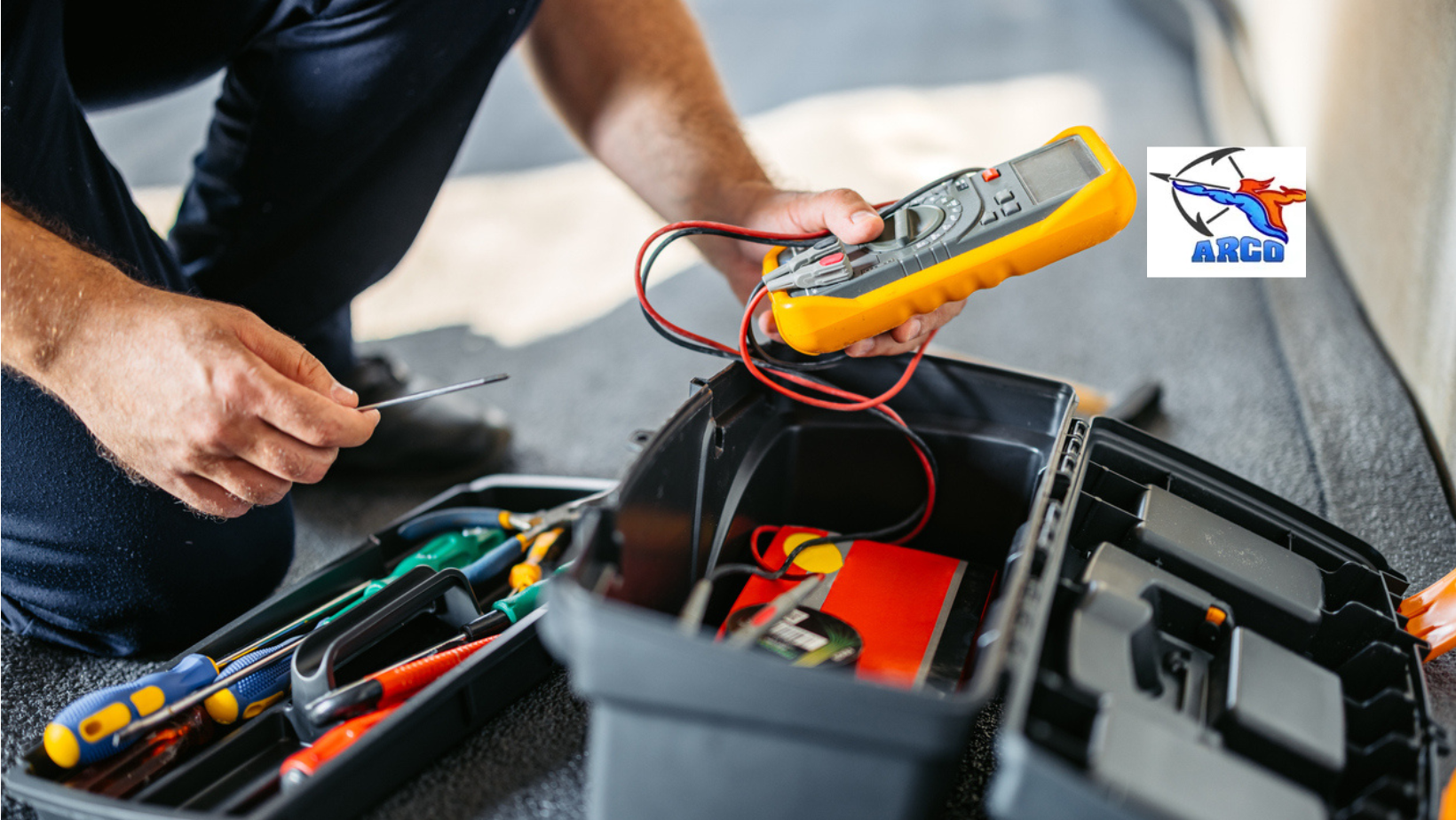 Electrician with tools, using a multimeter; toolbox open. ARCO.