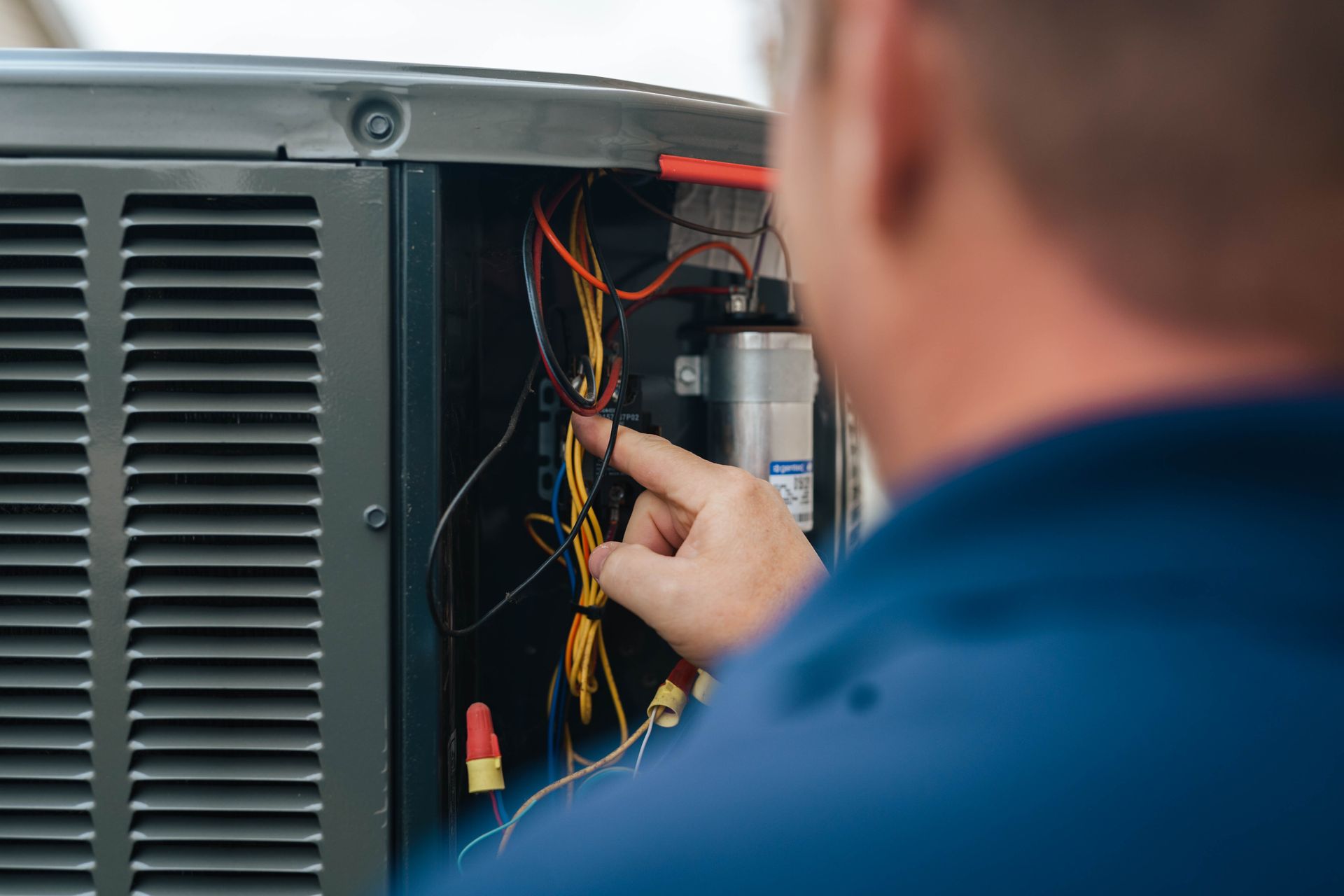 A man is working on an air conditioner and pointing at the wires.