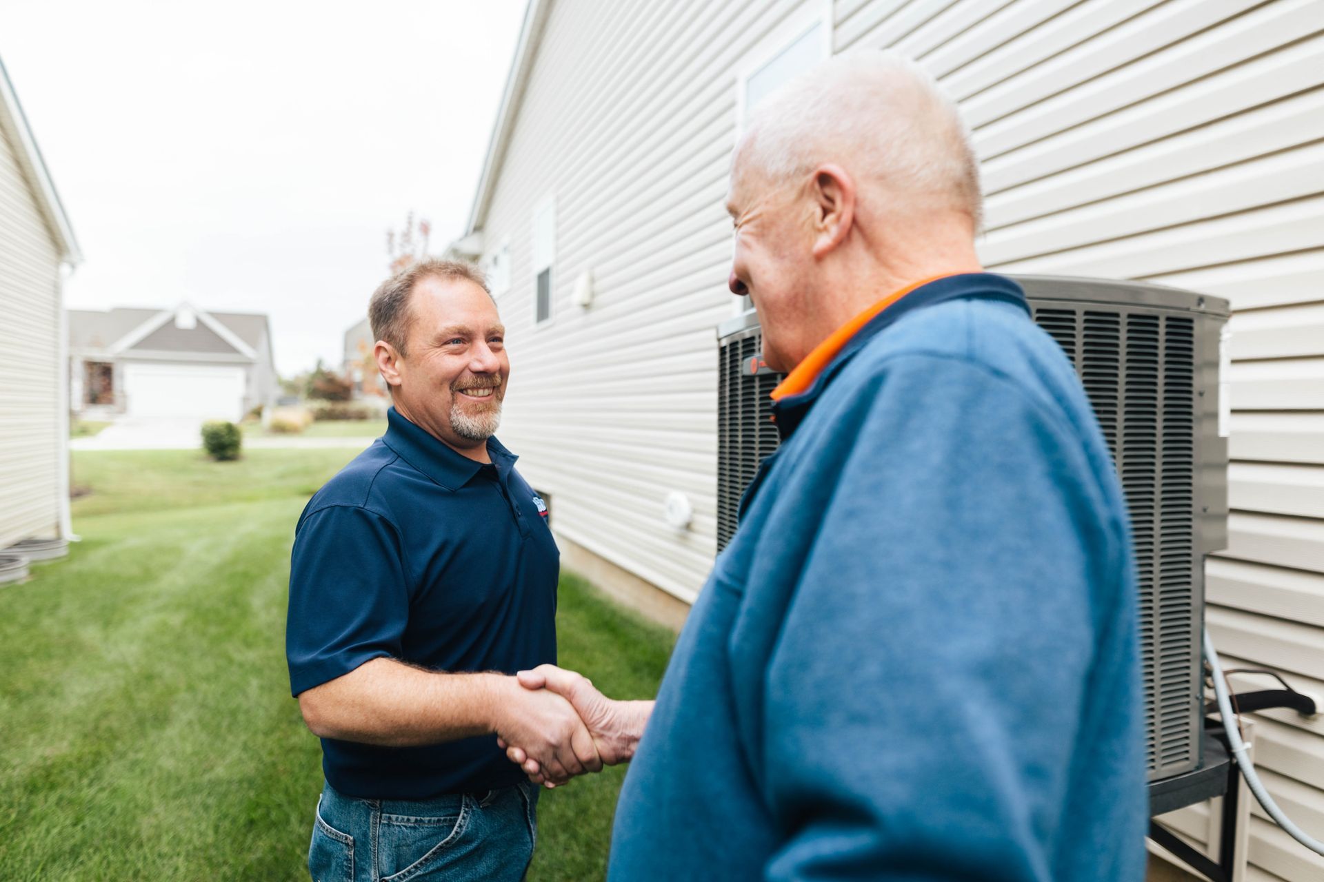 Two men are shaking hands in front of a house.