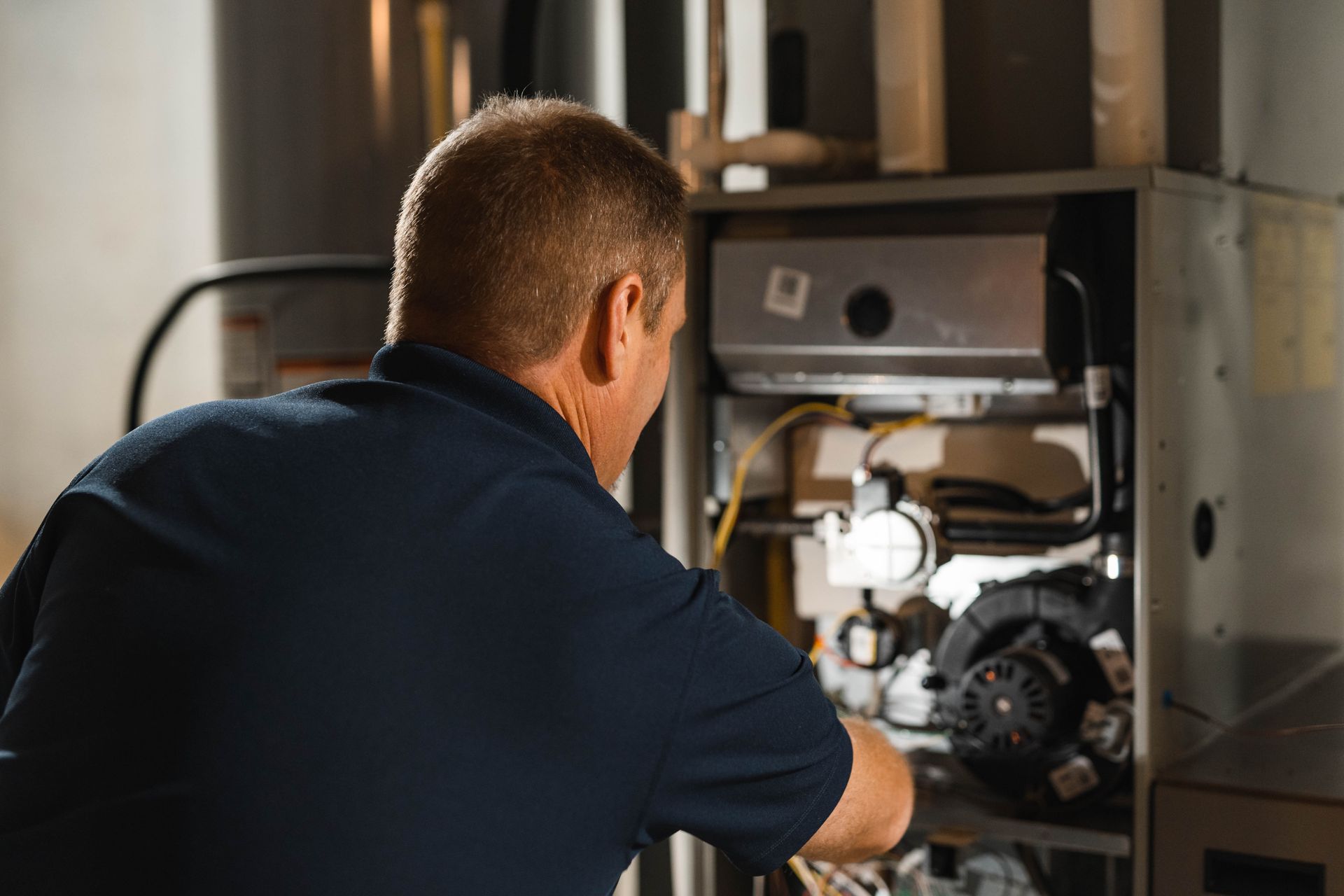 A man in a blue shirt is working on an air conditioner.