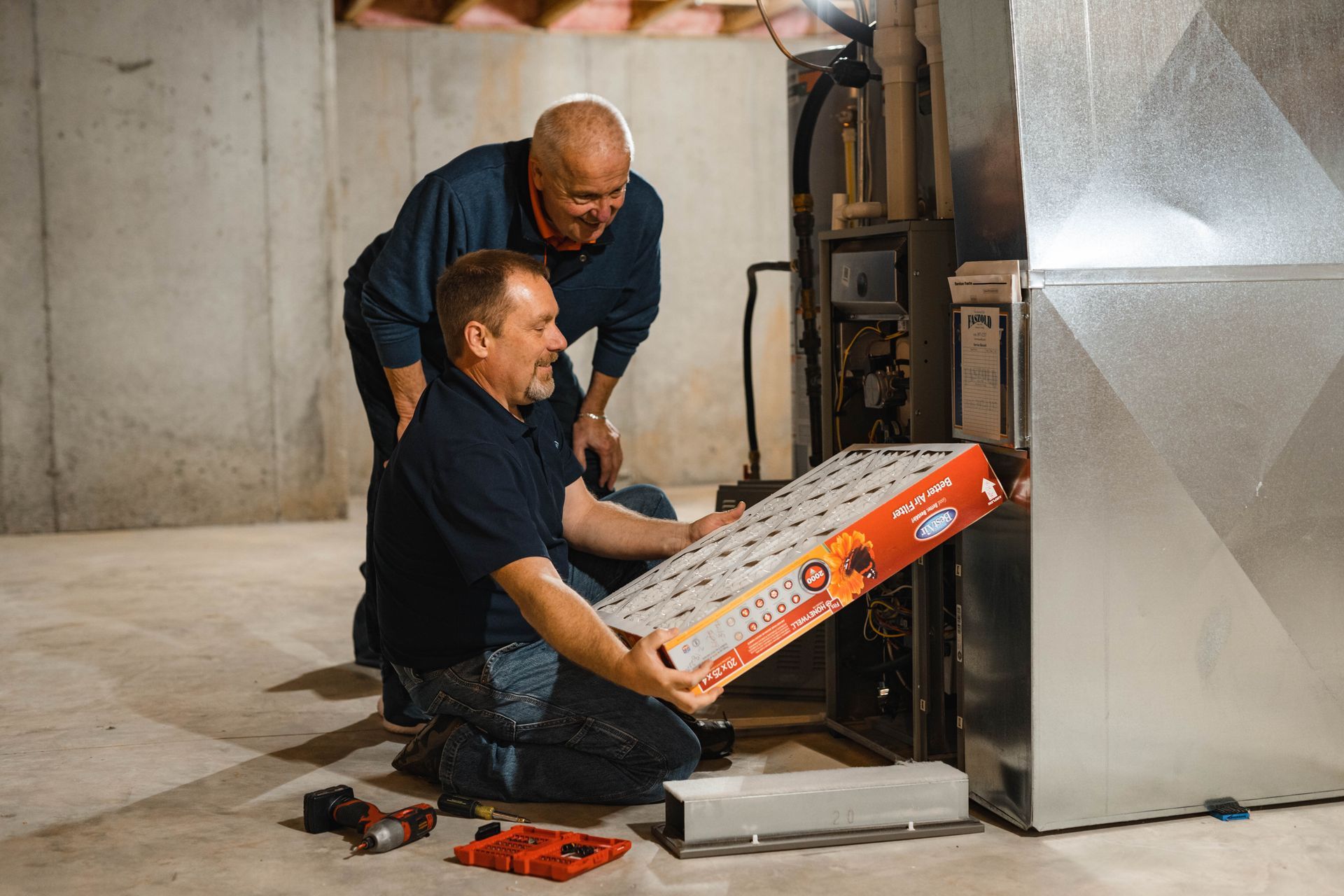 Two men are working on a furnace in a basement.