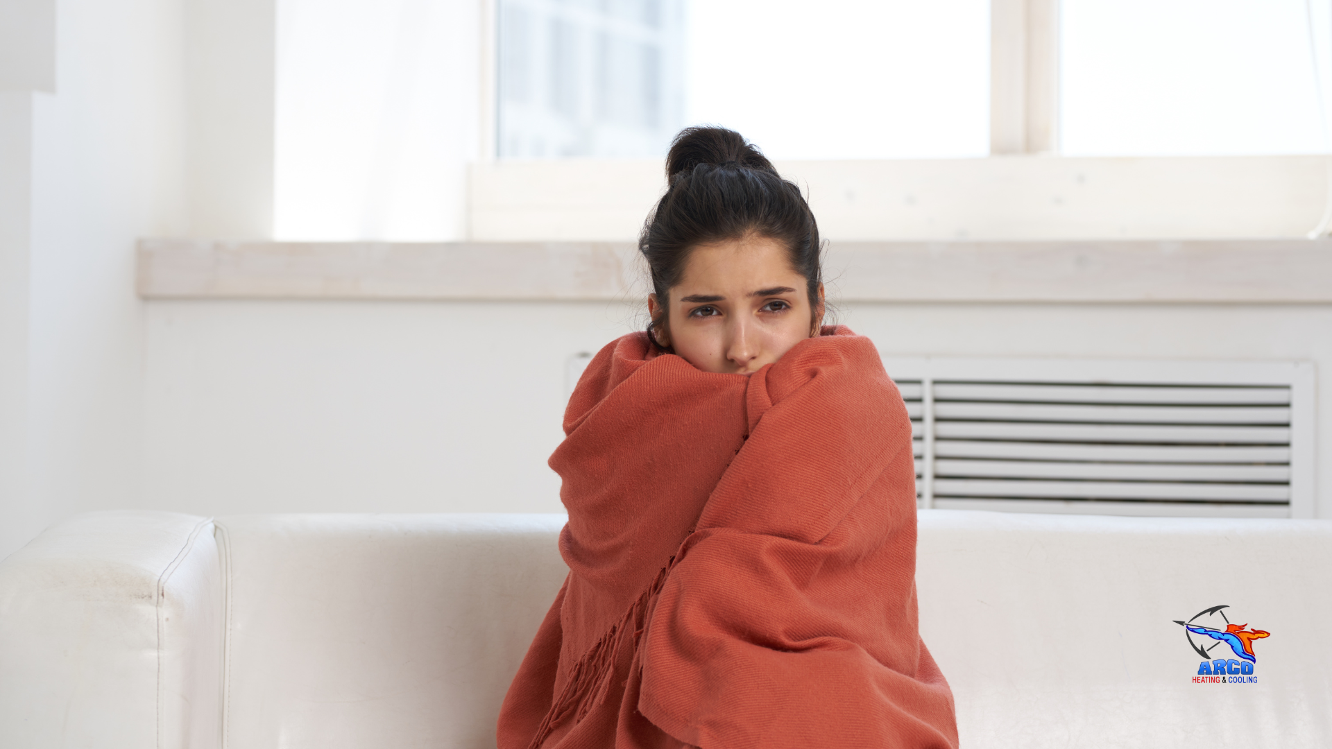 A woman wrapped in a blanket is sitting on a couch.