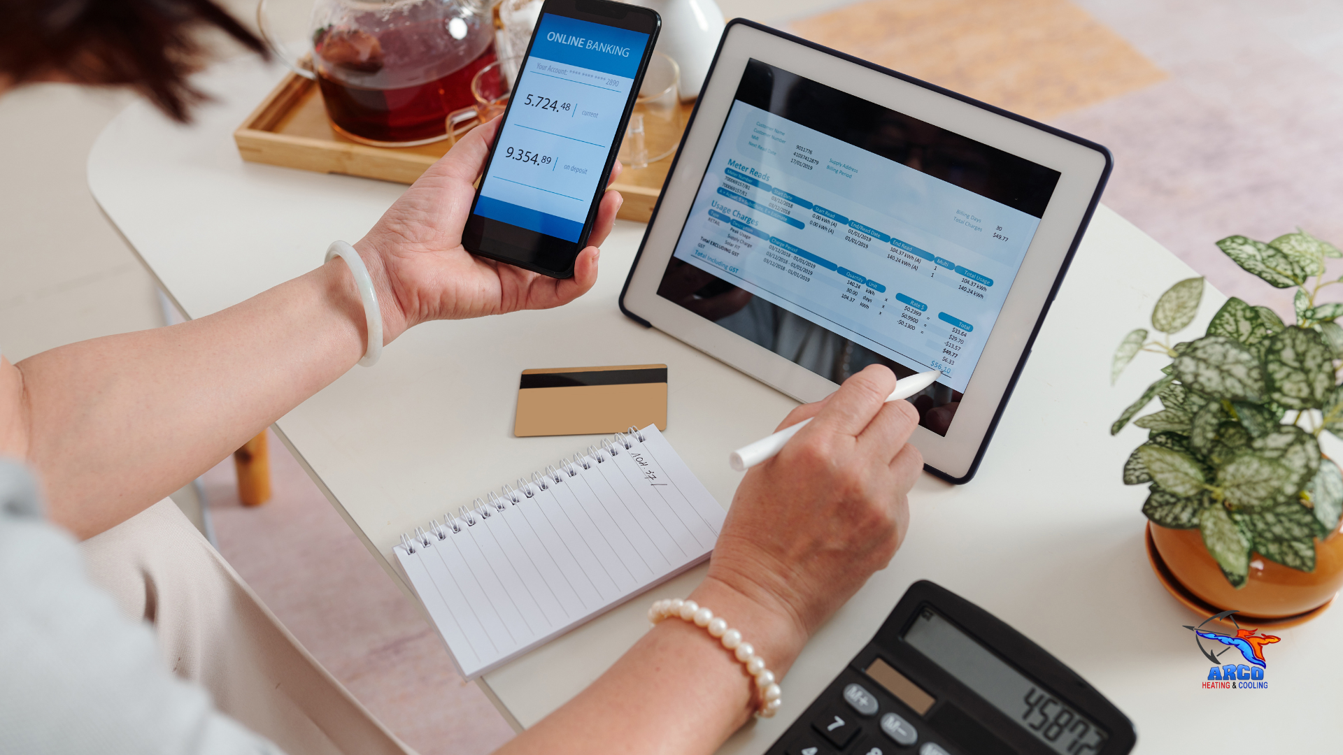 A woman is sitting at a table using a tablet and a cell phone.