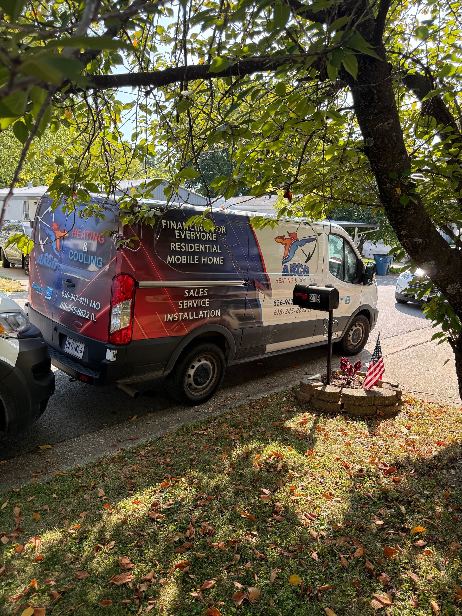 Branded van parked under trees beside a small flower bed in a leafy yard