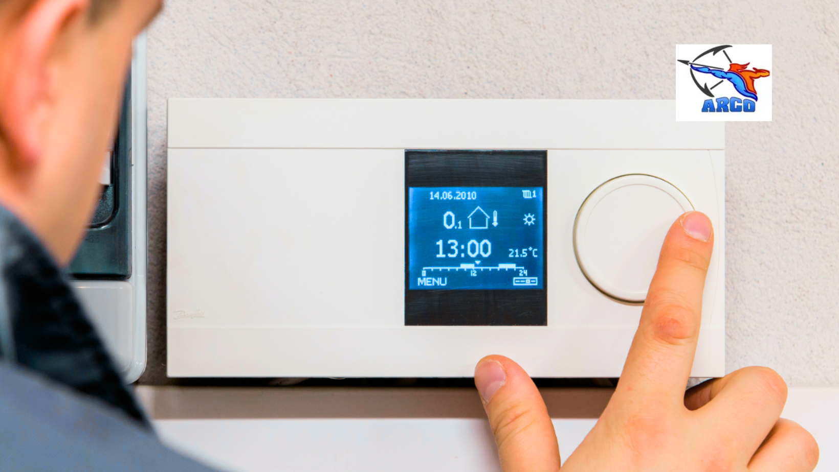 Hand adjusting a thermostat with a digital display showing 21°C and 13:00 on a wall panel