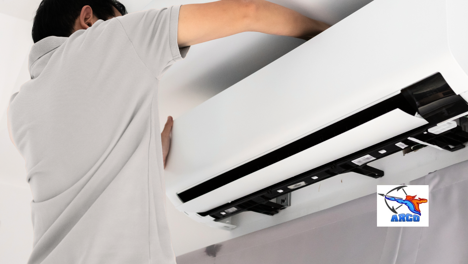 Person cleaning the underside of a wall-mounted air conditioner filter with a tool