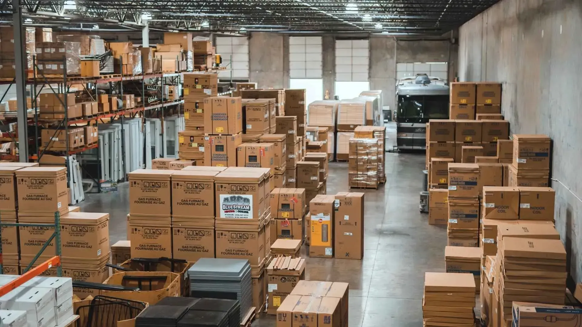 Warehouse aisle filled with stacked cardboard boxes and shelves of packaged goods