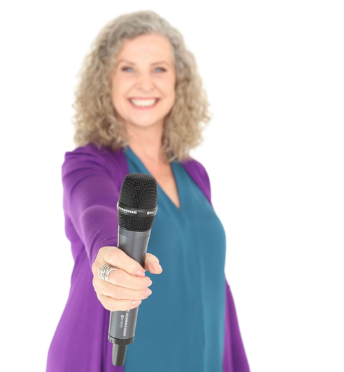 Woman smiling, holding out a microphone. Wearing purple cardigan over a teal top, white background.