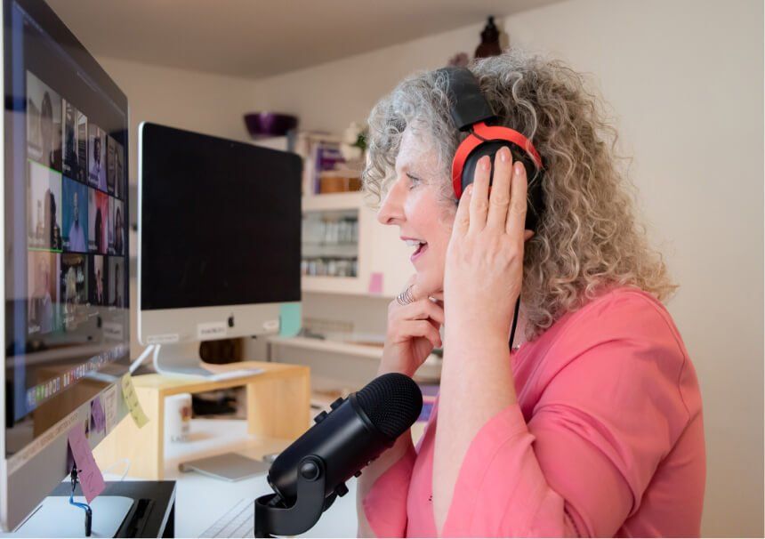 Woman wearing headphones, speaking into a microphone while looking at a computer screen with multiple video call