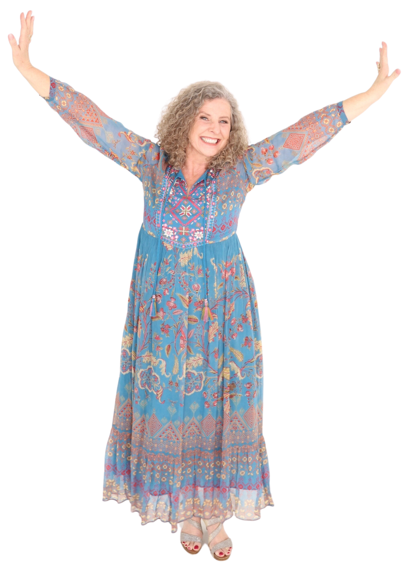 Woman in blue patterned dress with arms outstretched smiling.