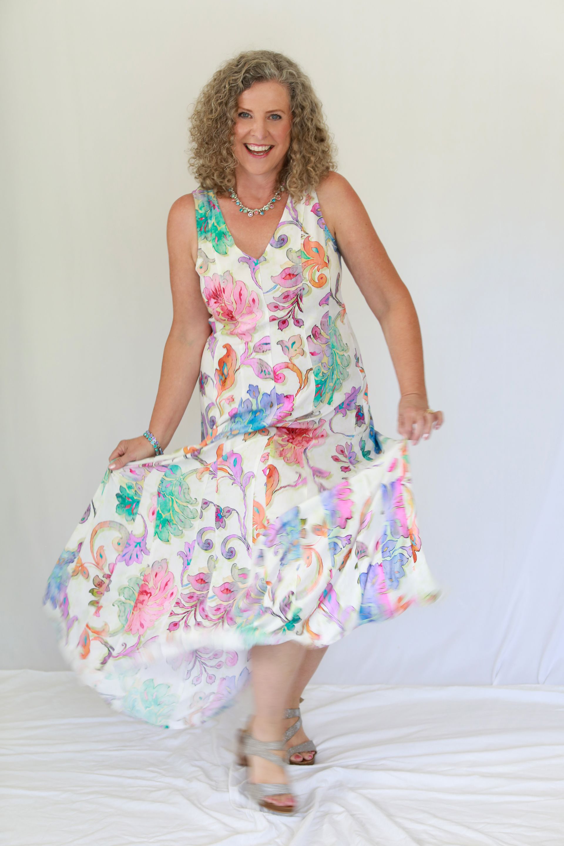 Woman in a floral dress twirling, smiling in front of a white backdrop.