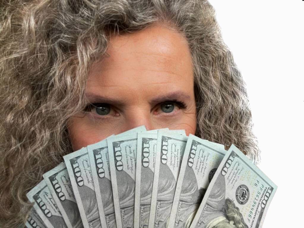 Woman holding a fan of $100 bills, peeking over them with a curious gaze.