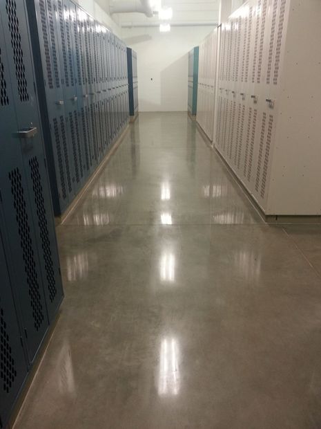 Long hallway lined with blue lockers on the left and white lockers on the right, with a shiny floor.